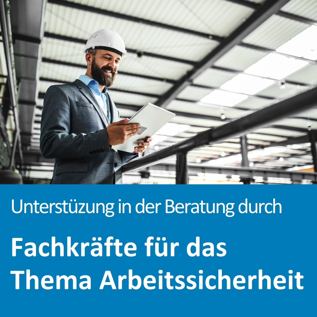 Ein lächelnder Mann mit Bart, Anzug und weißem Schutzhelm steht in einer modernen Industriehalle. Er hält ein Tablet in den Händen und wirkt konzentriert bei der Begehung oder Beratung zur Arbeitssicherheit. Die Umgebung ist geprägt von Stahlkonstruktionen und Tageslicht. Im unteren Bildbereich steht der Text: „Unterstützung in der Beratung durch Fachkräfte für das Thema Arbeitssicherheit“.